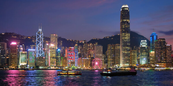 Hong Kong skyline cityscape downtown skyscrapers over Victoria Harbour in the evening illuminated with tourist boat ferries. Hong Kong, China